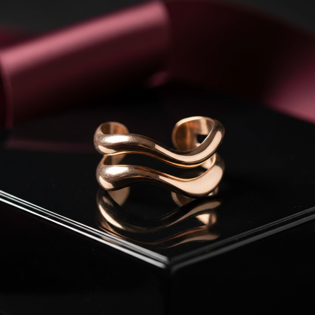 A dramatic close-up of a single sculptural ear cuff, crafted in polished rose gold with an organic, fluid, wave-like form that wraps in a double band. The cuff rests on the edge of a glossy black lacquer jewelry box, its reflective surface mirroring the metal’s warm hues. Behind it, out of focus, lies a blurred hint of a deep burgundy silk ribbon introducing a touch of color. Directional side lighting from the left creates striking highlights and defined shadows along the curves, emphasizing the piece’s three-dimensional form. The mood is bold, mysterious, and luxurious. Captured at a low, near-surface angle with a macro lens and extremely shallow depth of field, the cuff is rendered in hyper-real photographic detail, ideal for spotlighting a hero piece in a cutting-edge ear cuff collection.